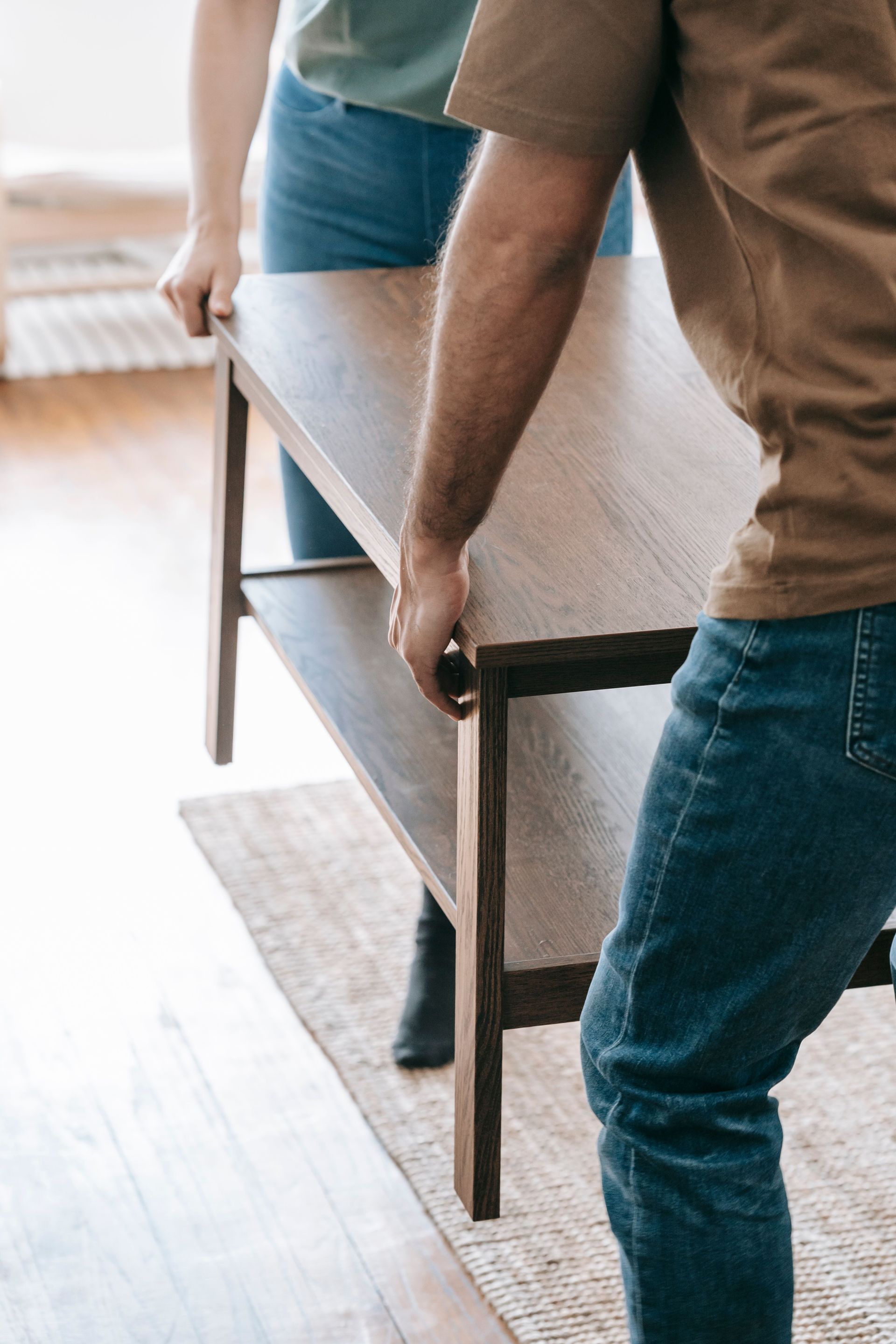 Couple gently lifting a wooden table in a bright indoor room, focusing on teamwork.